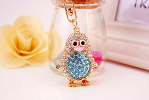 Macro detail of a golden penguin keychain featuring intricate blue and clear rhinestones