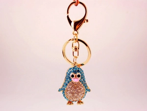 Close-up of golden penguin keychain with blue and clear rhinestones on pink background