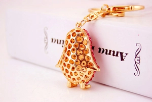 Close-up of golden penguin keychain featuring intricate honeycomb cutout and red rhinestones