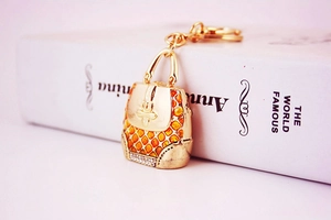 Detailed close-up of a gold alloy handbag keychain with orange enamel and shiny rhinestones