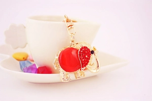 Detail of a golden elephant keychain with red rhinestones hanging on a white ceramic cup