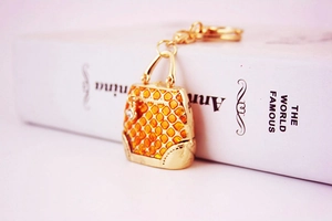 Close-up of golden mini handbag keychain with orange enamel and crystal details