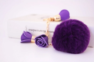 Detail shot of a dark purple plush ball keychain with a leather rose and gold metal clasp