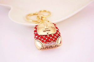 Close-up of golden metal handbag keychain with red enamel texture and white rhinestones