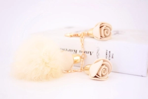 Detail of soft cream pompom and leather rose petals on a golden keychain