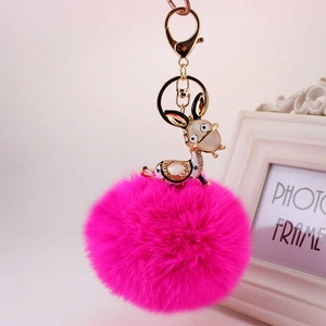 Detail of a bright pink faux fur pompom keychain with a golden rhinestone deer charm