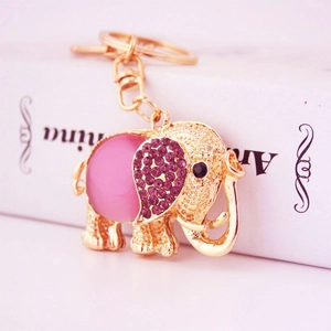 Golden elephant keychain with pink gemstone body and purple crystals on a white book