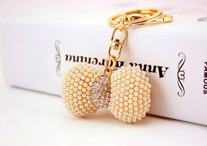 Detailed close-up of pearl bow keychain with crystals on golden metal hook and chain