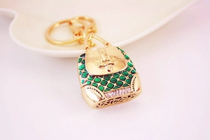 Detailed close-up of golden purse keychain with green enamel scales and white rhinestones
