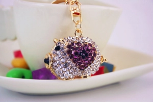 Detailed macro view of a sparkling rhinestone-paved cute pig keychain with purple heart decoration