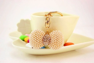 Detailed view of a gold bow keychain with white pearls and sparkling crystals on a cup