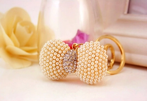 Detail of metal bow keychain with white pearls and sparkling rhinestone center