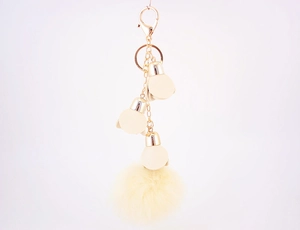Detail of a fluffy cream faux fur pompom keychain with golden metal clasp and chain