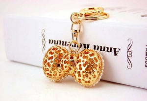 Detailed view of golden metal bow keychain with hollow patterns and white pearls decoration