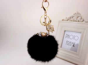 Close-up of black plush fur ball keychain with golden clasp and rhinestone donkey charm