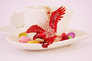 Detail of a golden eagle keychain with red rhinestones perched on a white ceramic cup