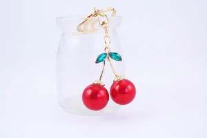 Close-up of a red cherry keychain with green crystal leaves and gold metal ring