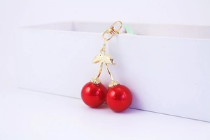 Detailed view of glossy red cherry keychain with gold-tone leaf and lobster clasp
