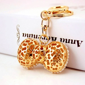 Elegant golden bow keychain with hollow patterns and pearls on a white book cover