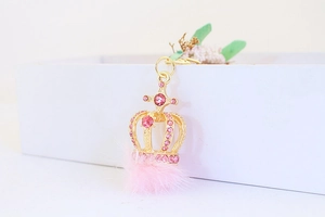 Detailaufnahme der goldenen Kronen-Schlüsselanhänger mit rosa Strasssteinen und Bommel