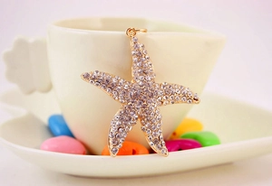 Close-up of a rhinestone starfish keychain hanging on a white ceramic cup with gold details