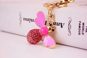 Detailed close-up of a golden bee keychain with pink enamel wings and magenta crystals
