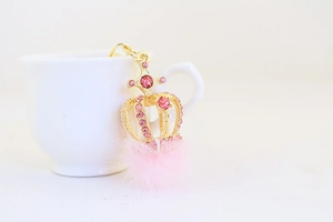 Detailaufnahme eines goldenen Kronen-Schlüsselanhängers mit rosa Steinen und flauschigem Pompon