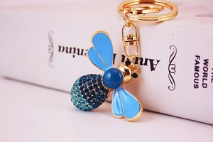 Macro detail of a bee keychain featuring blue crystals and light blue enamel wings