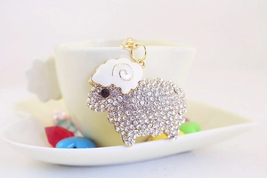 Detailed view of a gold-plated sheep keychain with sparkling rhinestones on a white cup