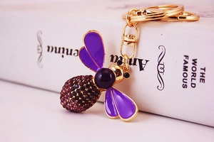 Close-up of a bee keychain with purple enamel wings and crystals on a book