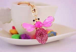 Detailed macro view of pink crystal rhinestone bee keychain on a white ceramic cup