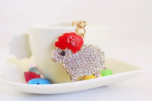Close-up of sheep keychain with sparkling rhinestones and red enamel on a white cup