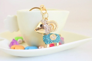 Close-up of a goat keychain with blue rhinestones hanging on a white ceramic cup