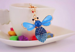 Detailed macro of a cute crystal bee keychain with blue rhinestone gradient on a white cup