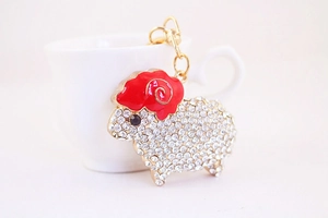 Detail of cute rhinestone sheep keychain with gold lobster clasp on white ceramic cup background