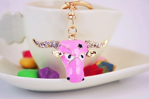 Detail of pink enamel bull head keychain with crystals hanging on a white coffee cup