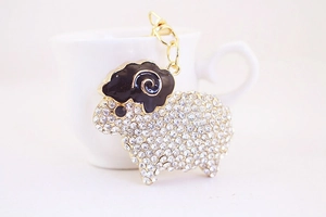 Detail of a sparkling sheep keychain with white rhinestones and golden horns on a white cup