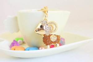 Macro detail of a golden sheep keychain with white and amber rhinestones on a coffee cup
