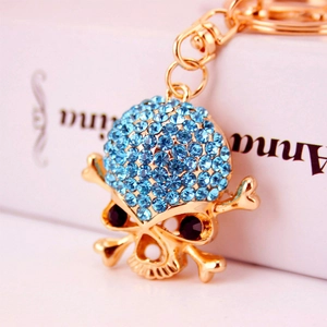 Portachiavi a teschio dorato con strass blu e occhi neri su sfondo bianco