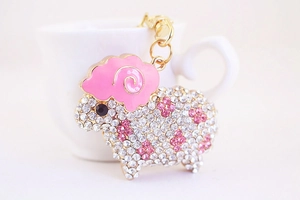 Close-up of sheep keychain with pink enamel and sparkling rhinestones on ceramic background