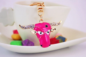 Detail view of pink enamel bull head keychain with white rhinestones on a white cup