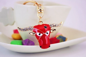 Close-up of red enamel bull head keychain with white rhinestones on white ceramic cup