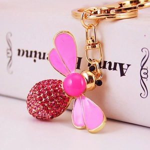 Pink bee keychain with red rhinestones and pearl head leaning on a white book