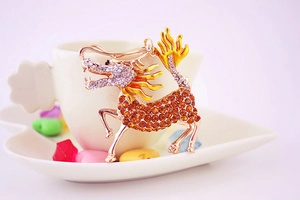 Detailed view of a golden Kirin pendant with yellow and white rhinestones on a white cup