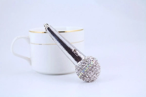 Close-up of a silver microphone keychain with sparkling rhinestones near a white ceramic cup