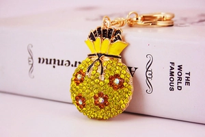 Close-up of golden money bag keychain with yellow rhinestones and floral enamel pattern