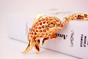 Detailed close-up of hollow fish keychain with pink rhinestones on a gold metal body