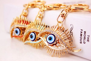 Three gold evil eye keychains with rhinestones and enamel details on white background