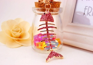Close-up of rose gold fishbone keychain with pink crystals on warm decorative background