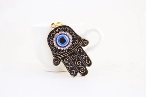 Macro shot of gold Hamsa hand keychain with black enamel and blue evil eye charm